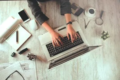 Blog image - looking from above down at a table with a laptop with hands typing, coffee and papers.