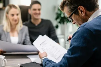 Financial adviser looking at filled in form on paper with couple sitting in the background