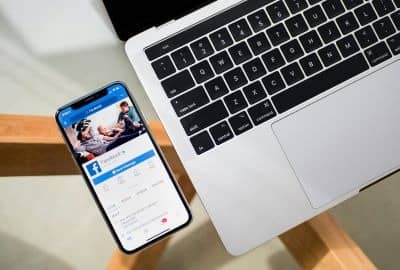 Phone screen with Facebook and a laptop on a table