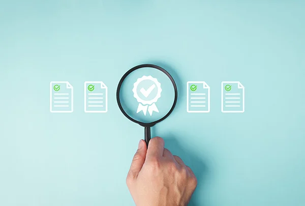 Hand holding magnifying glass inspecting certification icons